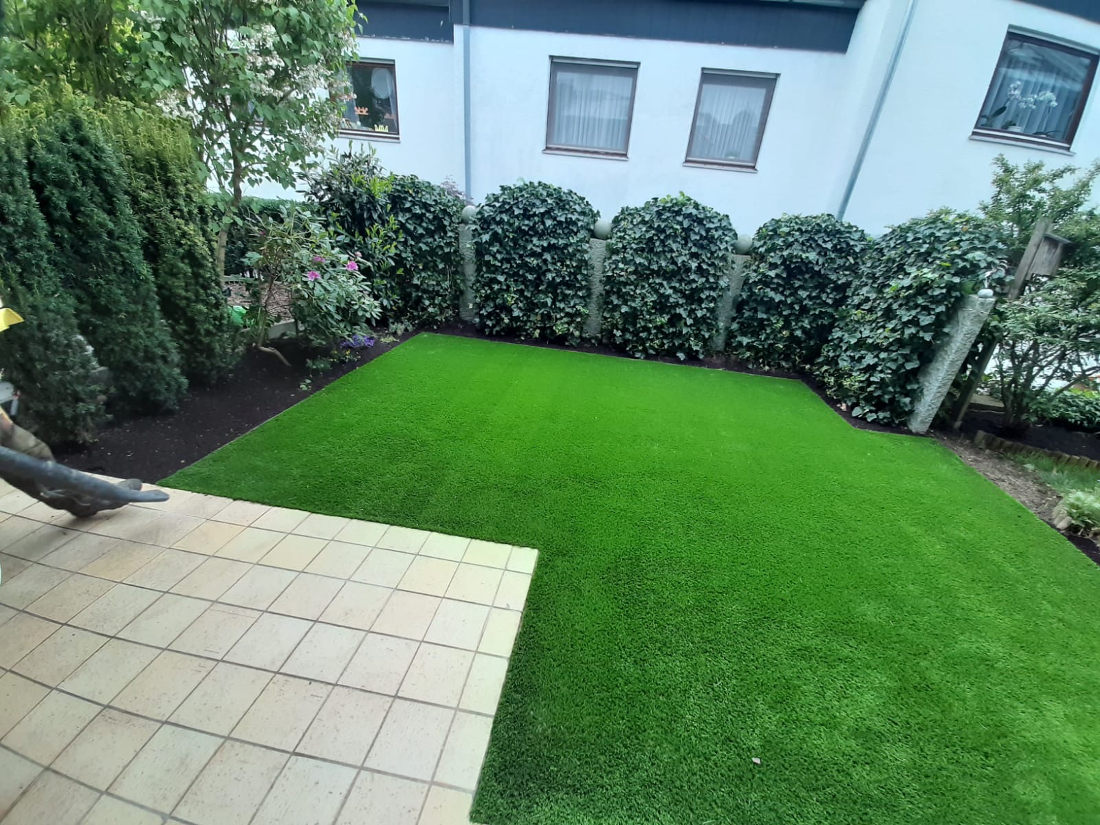 Kunstrasenfläche mit Pflasterterrasse im Vorgarten