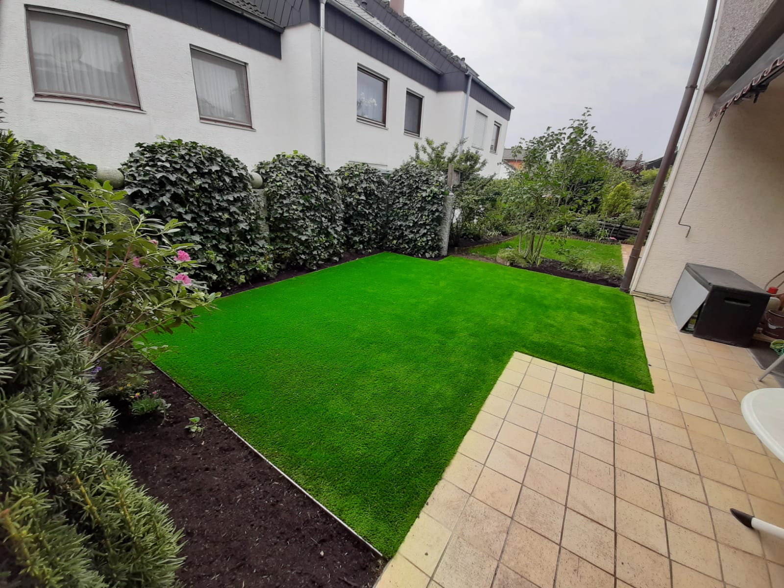 Seitliche Ansicht der Kunstrasenfläche mit angrenzender Pflasterterrasse und Beet in Stuttgart.