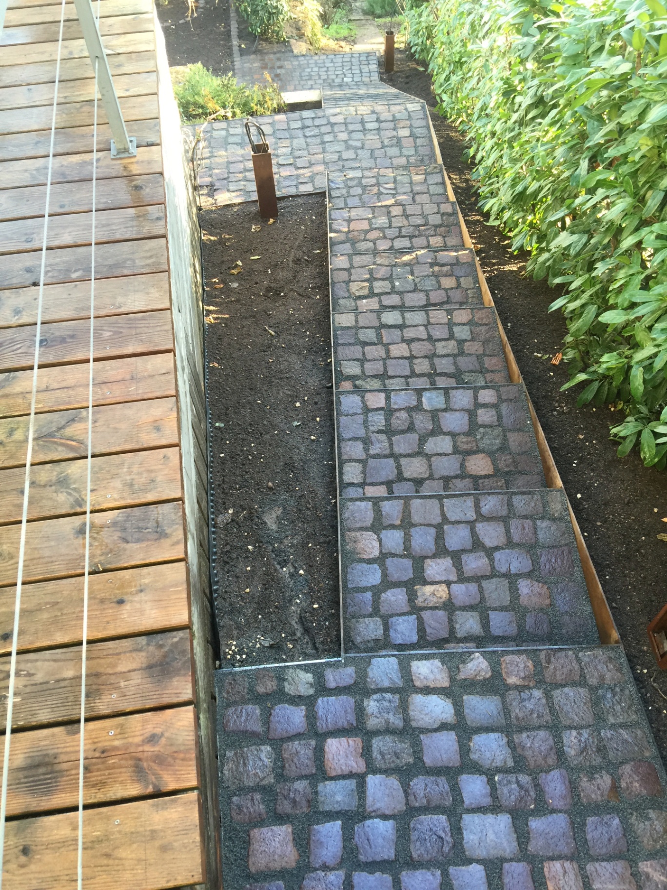 Natursteinpflaster und Wegeverlauf entlang der Holzterrasse