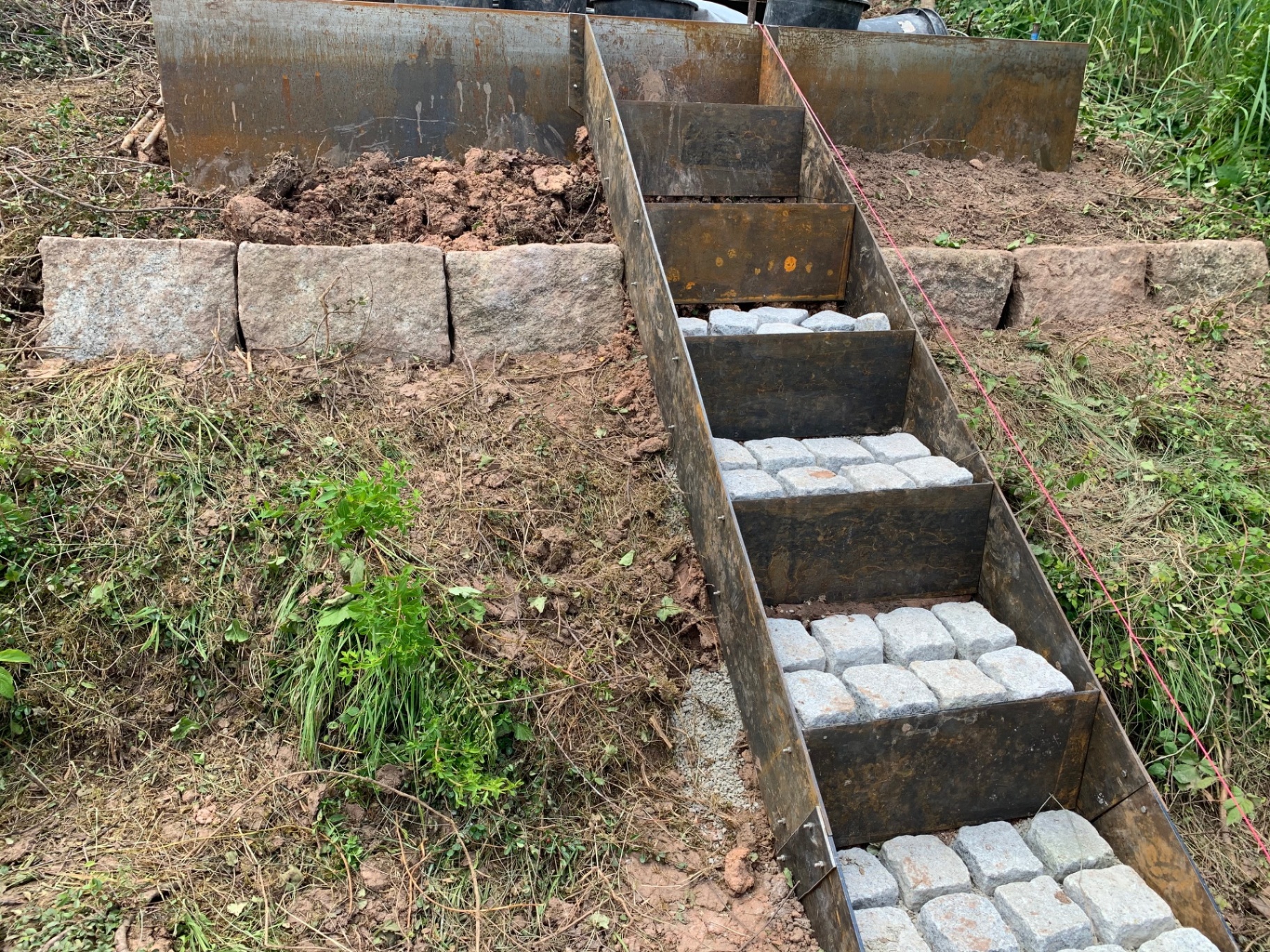 Bauphase der Hangtreppe mit weiter geführter Stahleinfassung und Natursteinpflaster