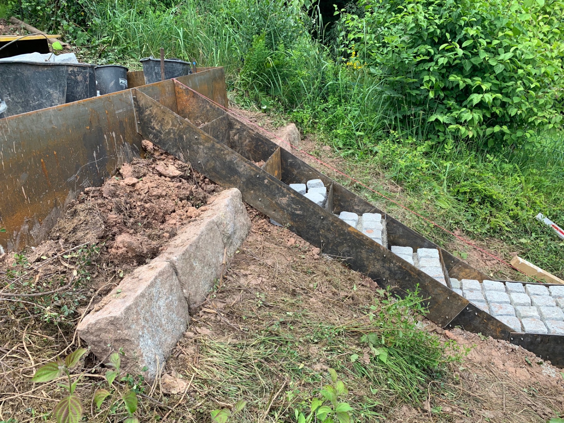 Seitliche Detailansicht der Hangtreppe während der Ausführung mit Stahleinfassung und Natursteinpflaster