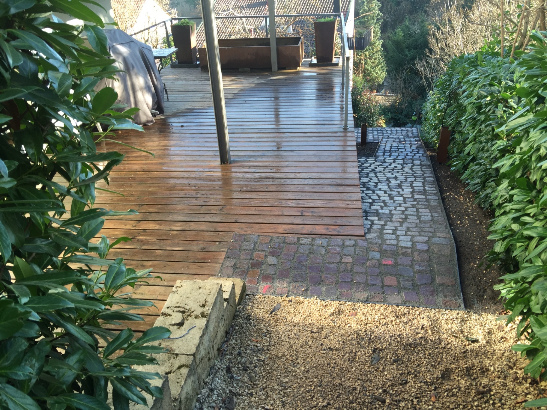 Holzterrasse mit Anschluss an Pflasterflächen in einer Gartenanlage in Hanglage
